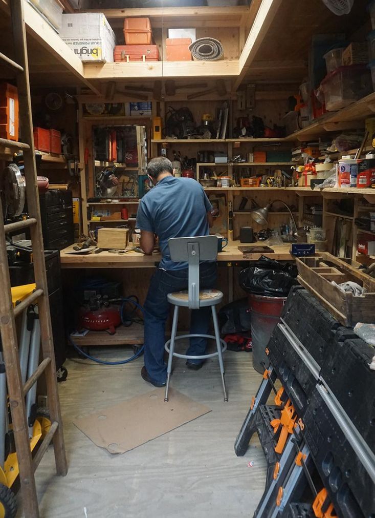 a man working in a workshop with lots of work on the table and shelves full of tools