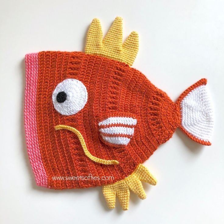 a crocheted fish hat is shown on a white surface with an orange and yellow stripe