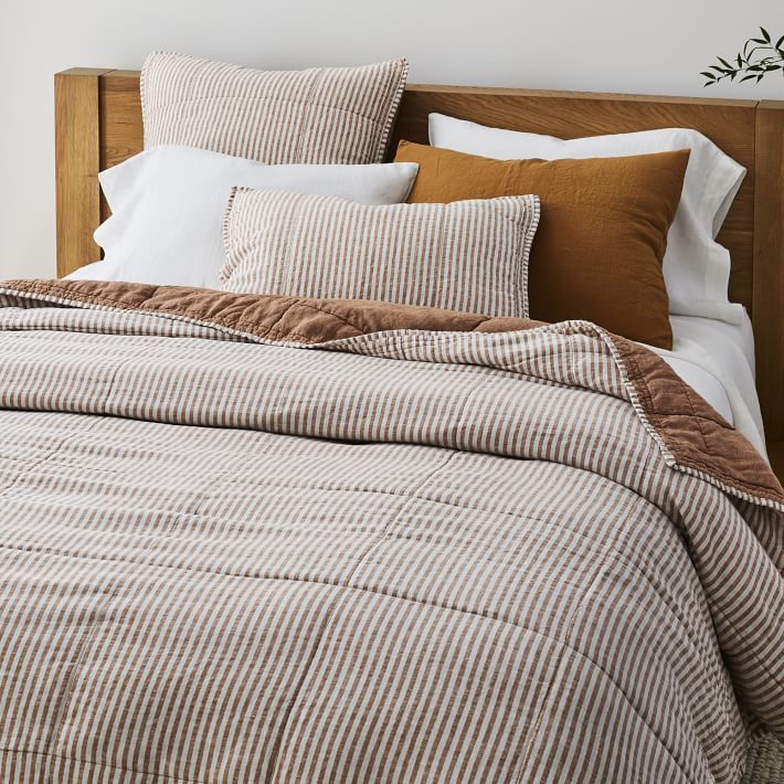 an unmade bed with brown and white striped comforter