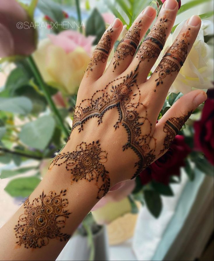 a woman's hand with henna tattoos on it and flowers in the background