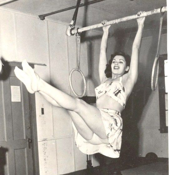 a woman hanging upside down with a tennis racquet in her hand while holding onto the bar