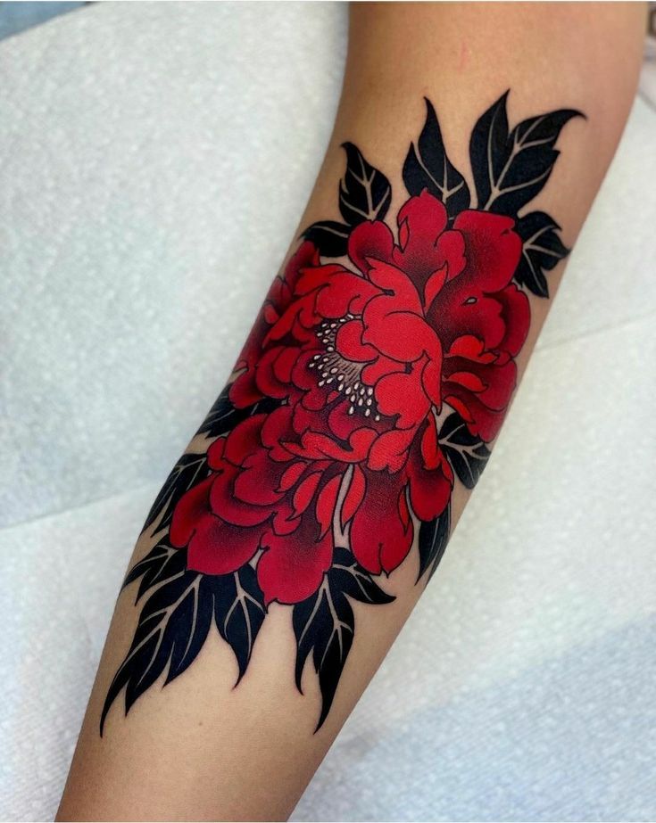 a woman's arm with red flowers and black leaves on the bottom half of her arm