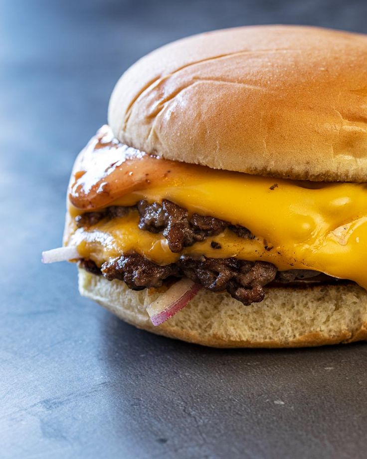 a cheeseburger with meat and onions is on a blue countertop, ready to be eaten