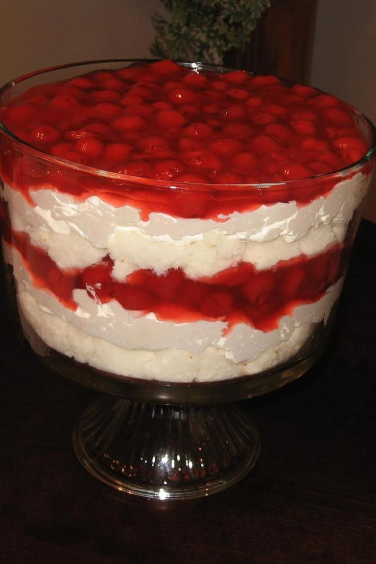 a red and white layered cake on a glass platter with silver serving utensils