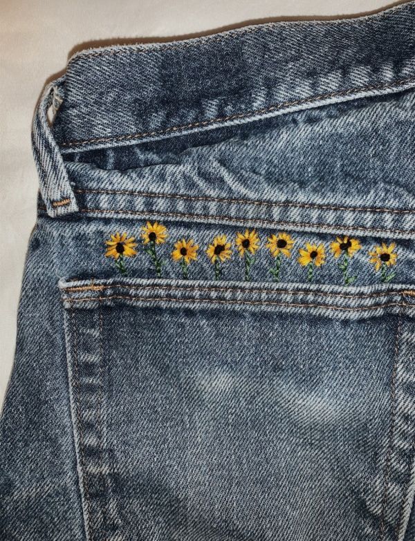 the back pocket of a pair of jeans with embroidered sunflowers on each side