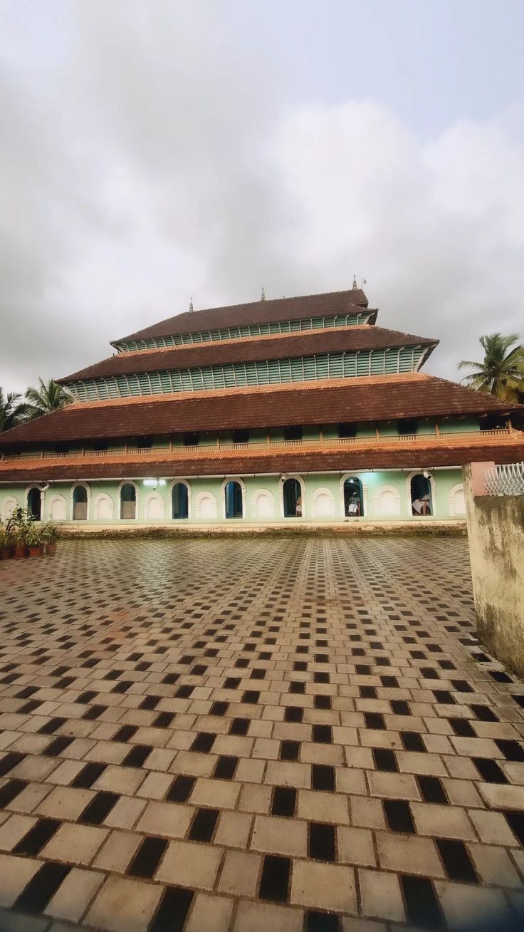 an old building with a tiled floor in front of it and palm trees behind it