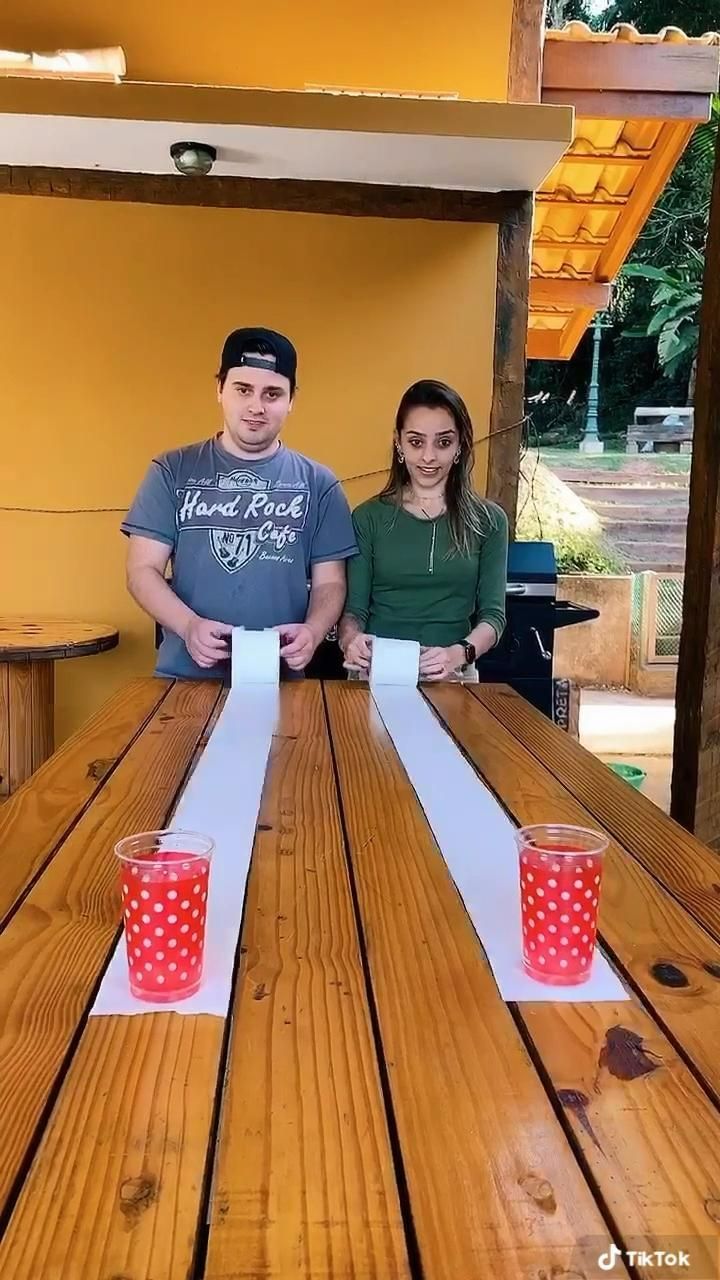 two people sitting at a picnic table with paper on it and cups in front of them