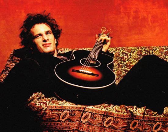 a man sitting on top of a couch holding an acoustic guitar in his right hand