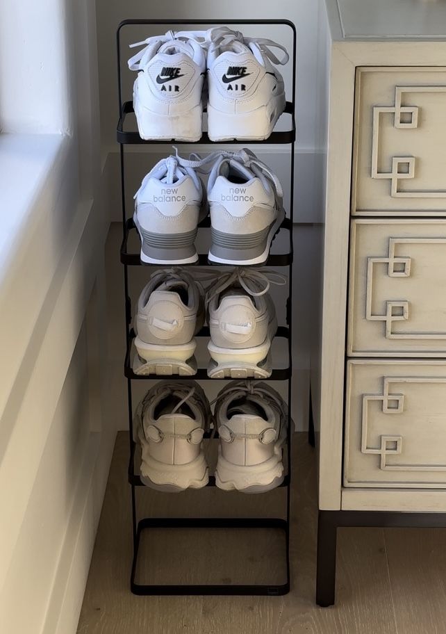 several pairs of white shoes are on a black rack in the corner of a room