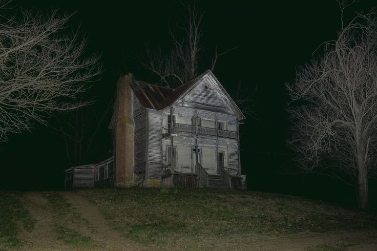 an old house sitting on top of a hill at night with trees in the background