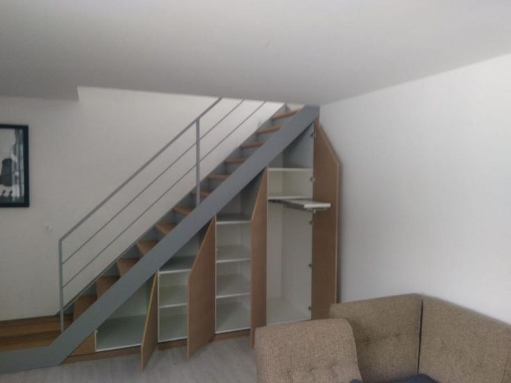 a living room with a couch, book shelf and stairs in the wall next to it