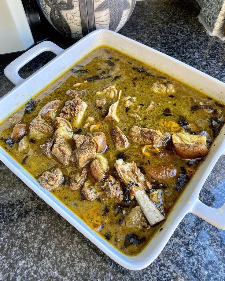 a white casserole dish filled with meat and vegetables sitting on a granite counter