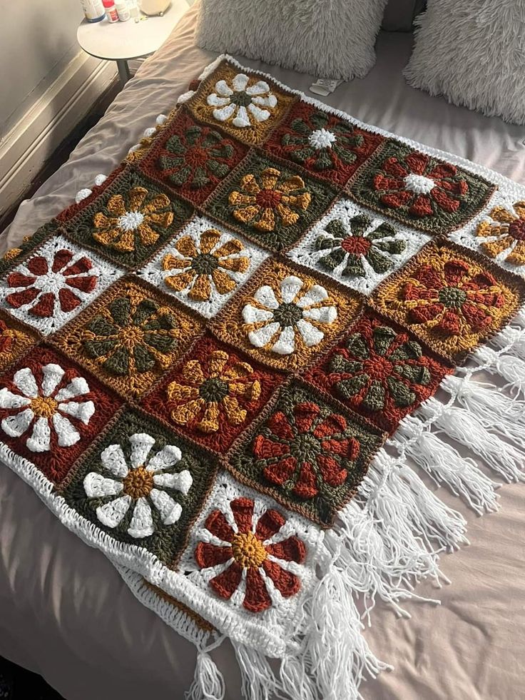 a crocheted blanket on a bed with white and red flowers in the center