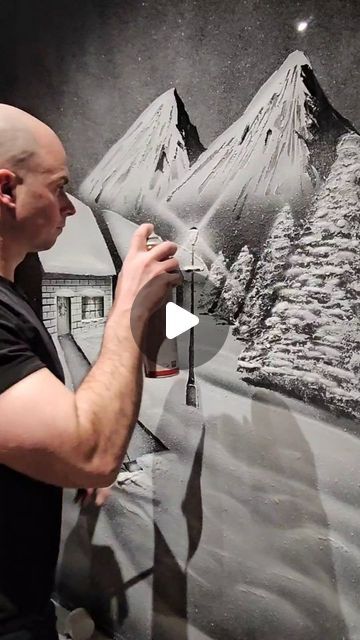 a man is painting a mountain scene on a wall with black and white paint in front of him