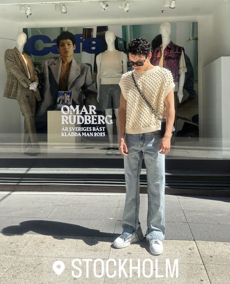 a man standing on the sidewalk in front of a store window with mannequins behind him