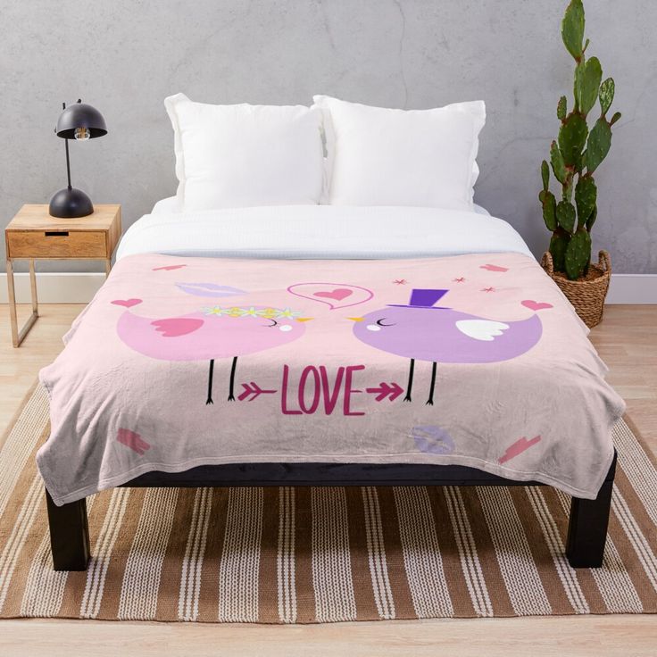 a bed with a pink blanket that says love and two birds on the top of it