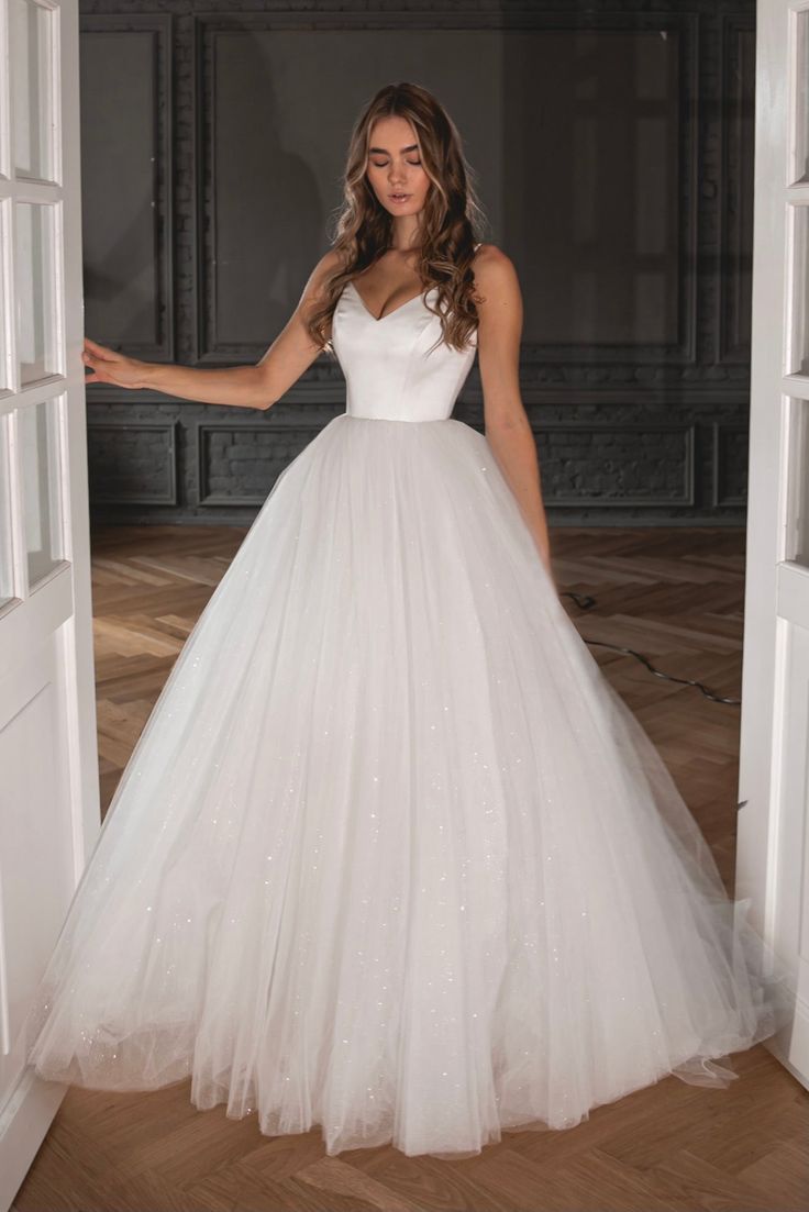 a woman in a white wedding dress standing by an open door with her hand out