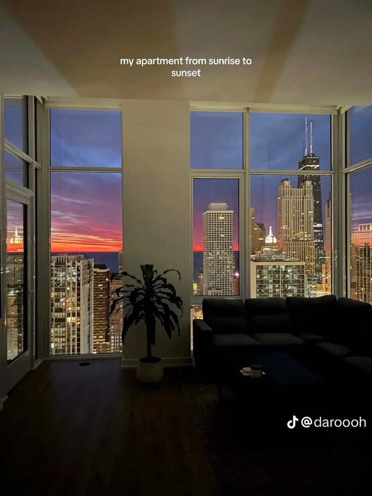 a living room filled with furniture and large windows overlooking the city at sunset or dawn