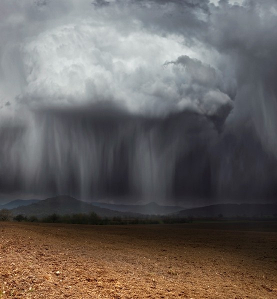 an image of a storm coming in from the sky over a dirt field and mountains