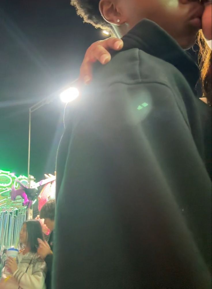 a woman standing in front of a carnival at night with her hand on the jacket