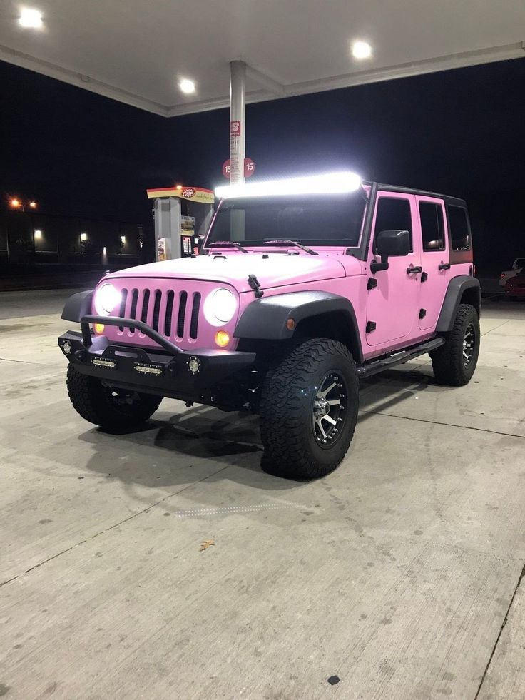 a pink jeep parked in front of a gas station at night with its lights on