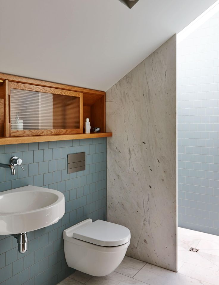 a white toilet sitting next to a bathroom sink under a wooden shelf above it's mirror