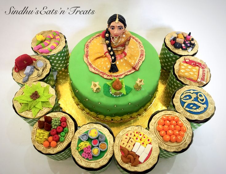 there is a green cake with many cupcakes around it and a woman's face on top