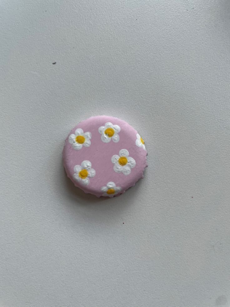 a pink button with white and yellow daisies on it sitting on top of a table