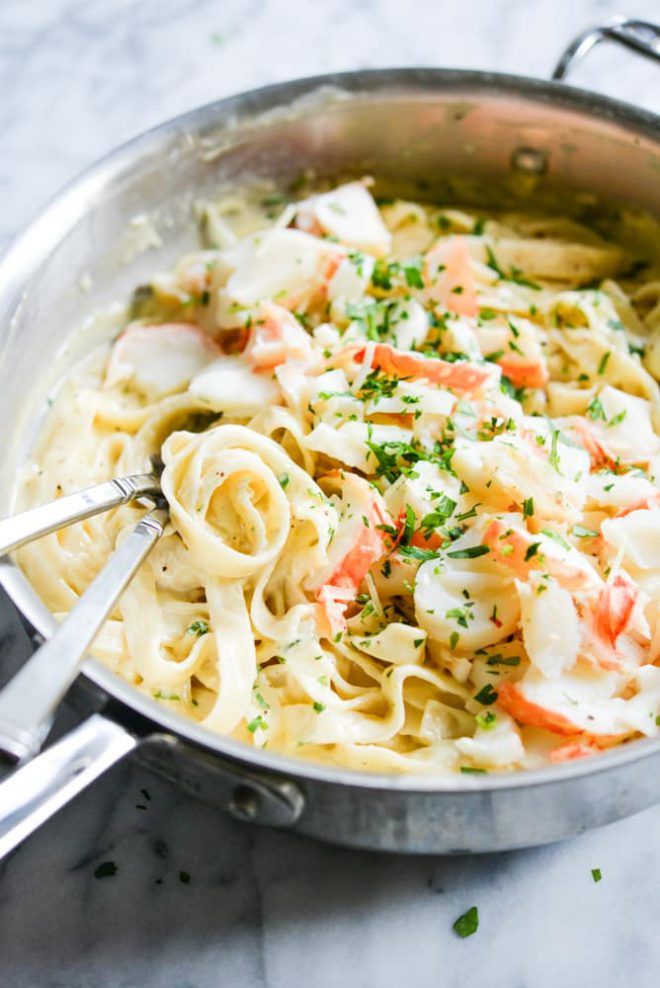 a pan filled with pasta and vegetables on top of a marble countertop next to silver utensils