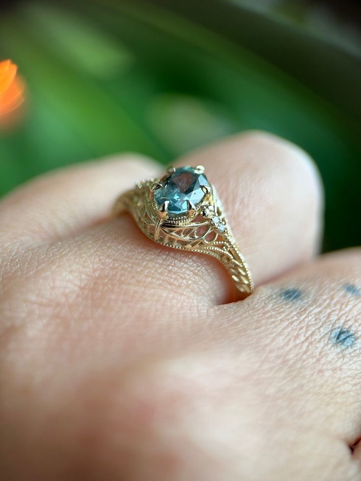 a close up of a person's hand holding a ring with a blue stone