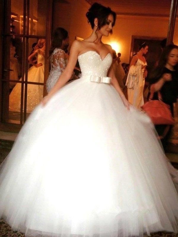 a woman in a white wedding dress is standing on the floor with other people behind her