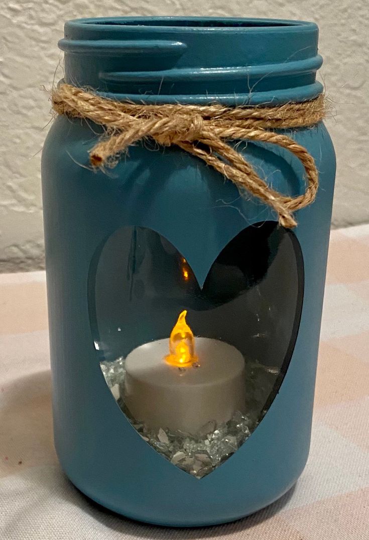 a blue mason jar with a lit candle inside and a heart shaped hole in it