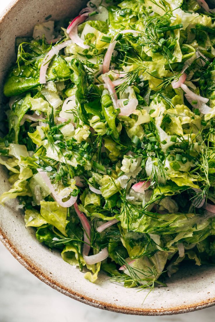 a white bowl filled with lettuce and onions on top of a marble counter