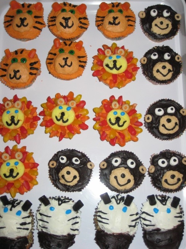 there are many cupcakes decorated with animals and lions on the top one is orange