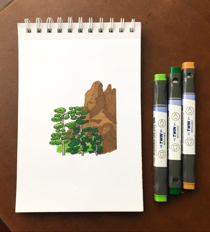 two markers are next to a drawing of a tree and mountains on a white paper