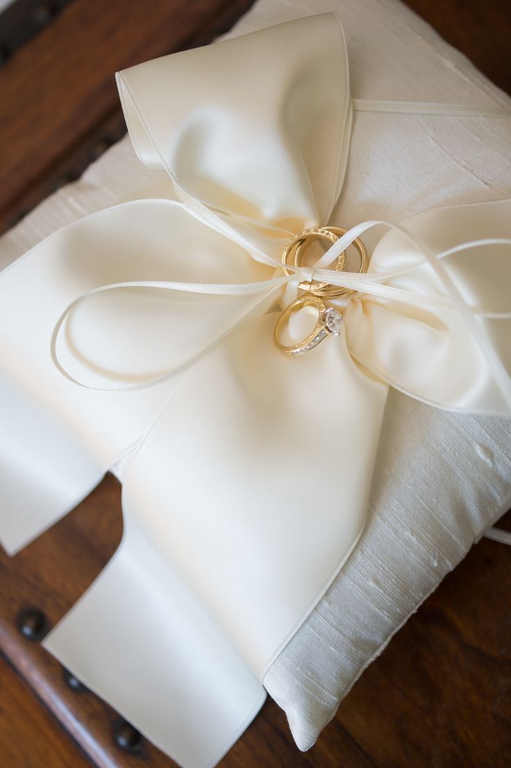 a ring pillow with a satin bow on it sitting on top of a wooden table