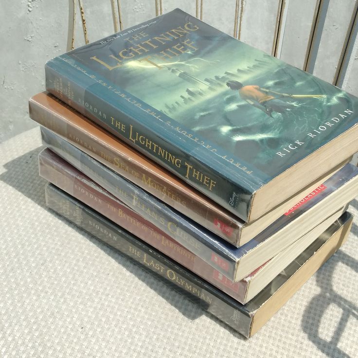 a stack of books sitting on top of each other next to a metal chair with a white wall in the background