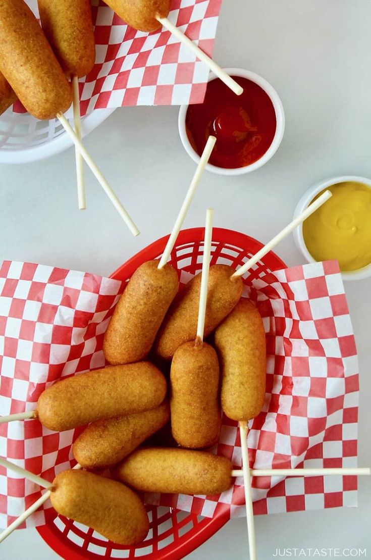 some fried food on sticks in a basket with ketchup, mustard and mayonnaise