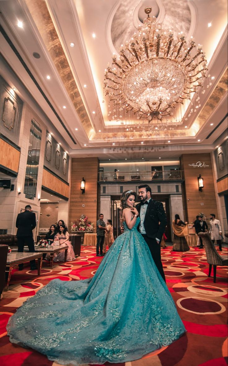 a bride and groom pose in front of a chandelier at their wedding reception