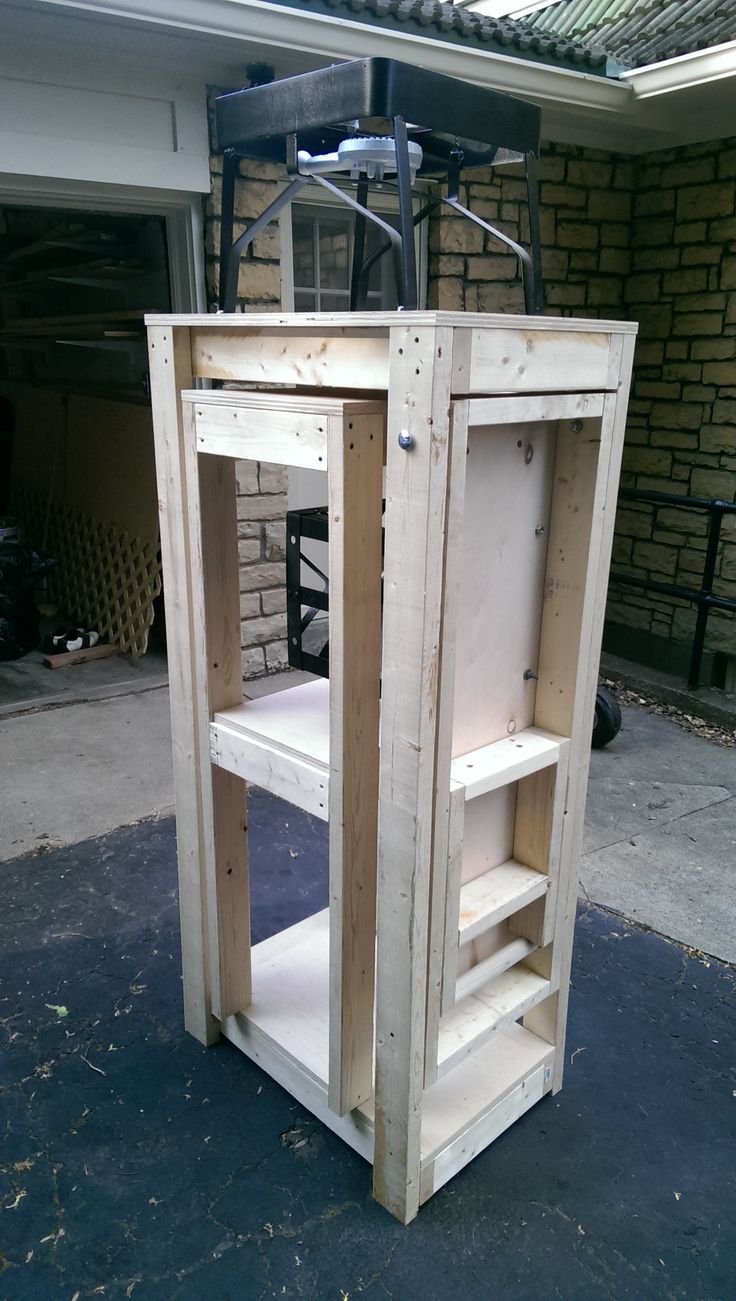 a wooden cart with two shelves on the top and one shelf below it, in front of a brick building