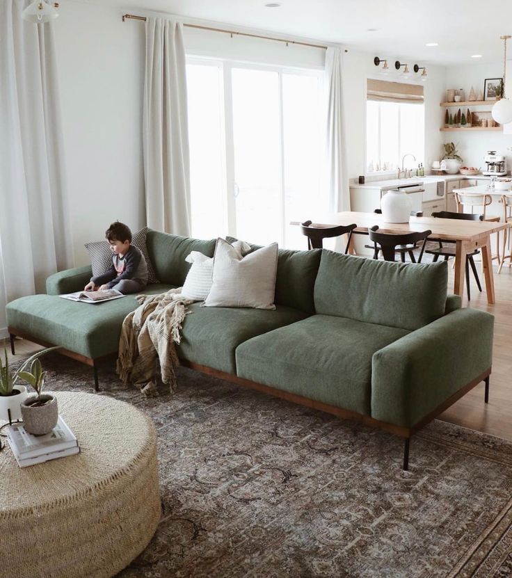 a woman sitting on top of a green couch in a living room next to a table