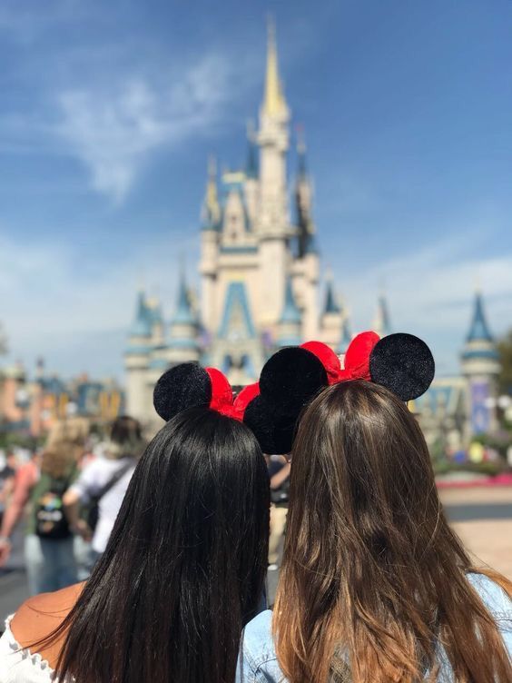 two girls wearing minnie mouse ears looking at the disney castle in front of their heads