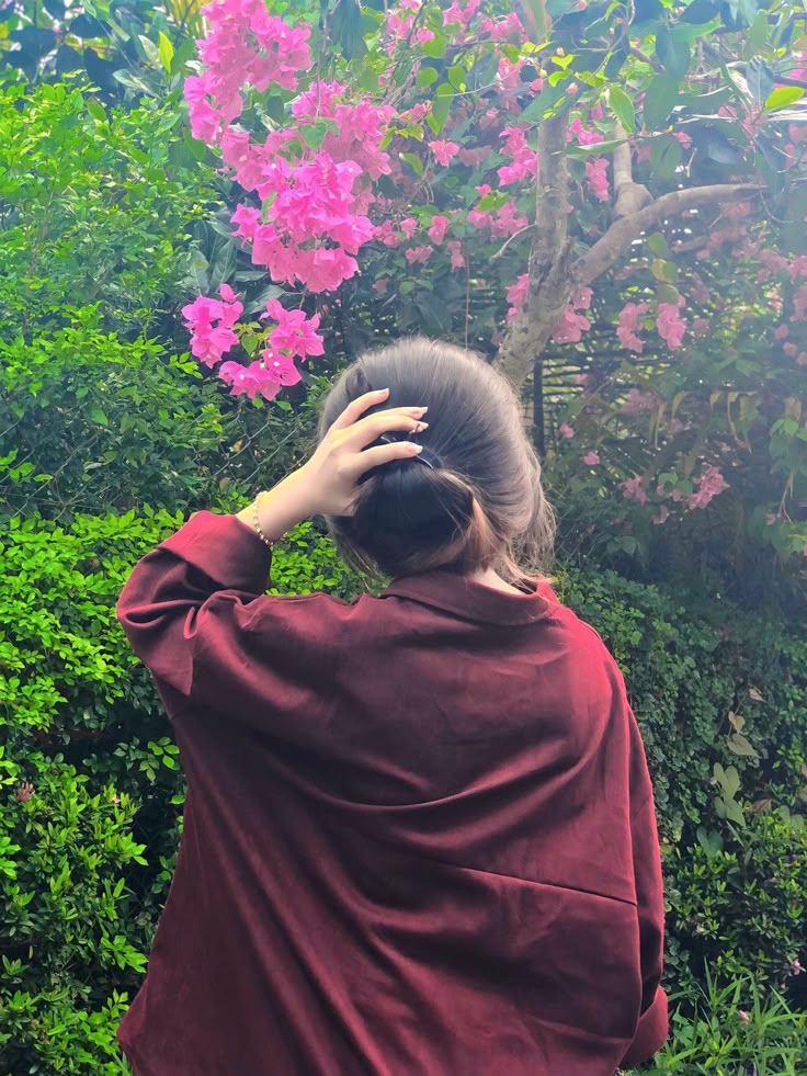 a woman in a red robe is looking at pink flowers