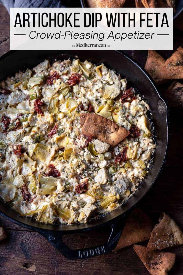 an artichoke dip with feta in a cast iron skillet surrounded by crackers