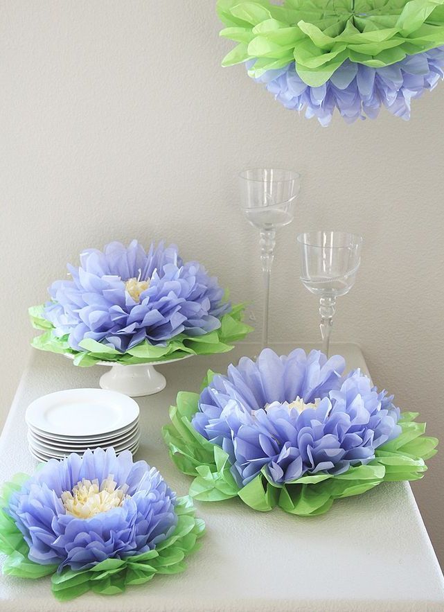 blue and green paper flowers are on display in front of wine glasses, plates and cups