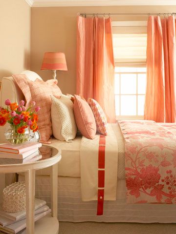 a bedroom with pink and orange decor on the bed, nightstands and window in the corner