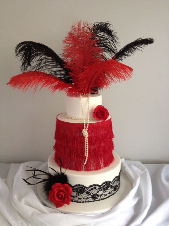 a three tiered cake with red feathers and flowers on the top is adorned with black lace