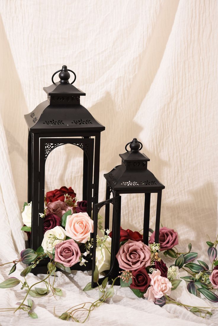 two black lanterns with pink and red flowers on them sitting next to each other in front of a white backdrop