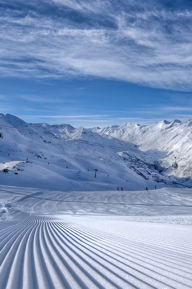 a person riding skis down a snow covered slope in front of a mountain range