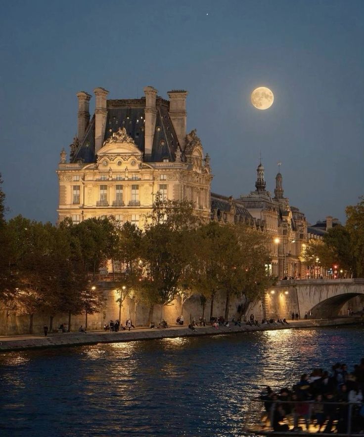 the full moon is setting over an old building on the riverbank in paris, france